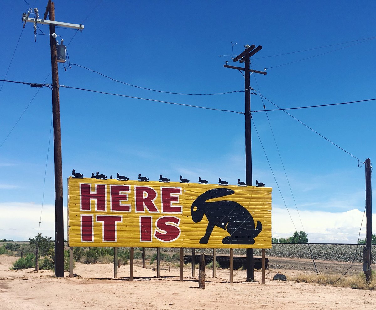 A yellow billboard with “Here it is” in red letters and a painted black jackrabbit