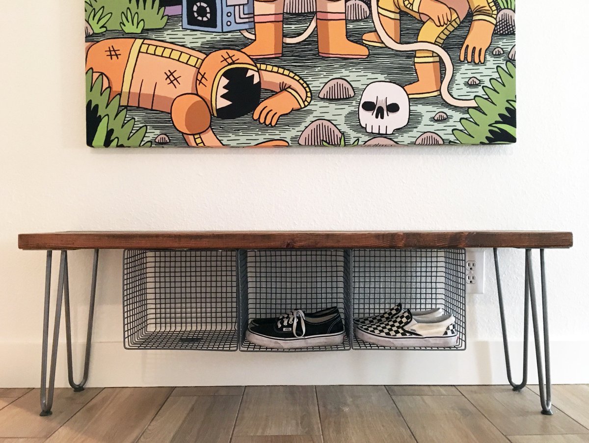 A wood bench with hairpin legs and metal wire baskets mounted underneath to hold shoes.