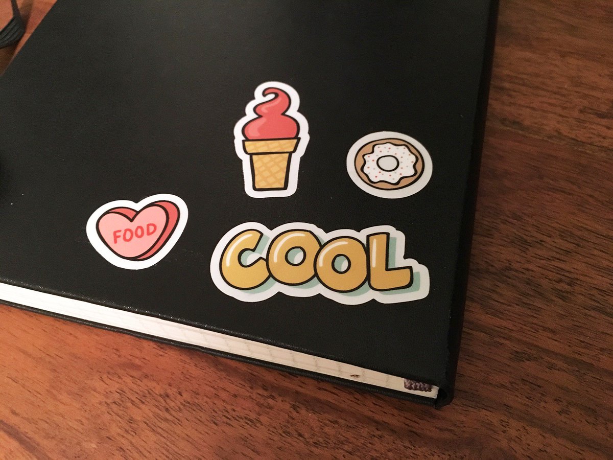 A moleskine notebook with stickers: a candy heart that says FOOD, a frozen yogurt cone, a donut, and the word COOL.