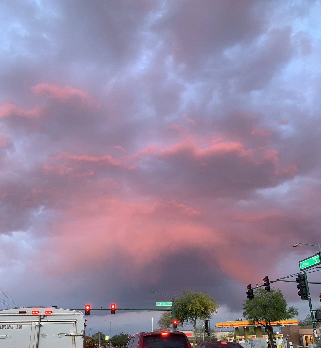 A street intersection below huge fluffy clouds in dark blues and bright pinks.