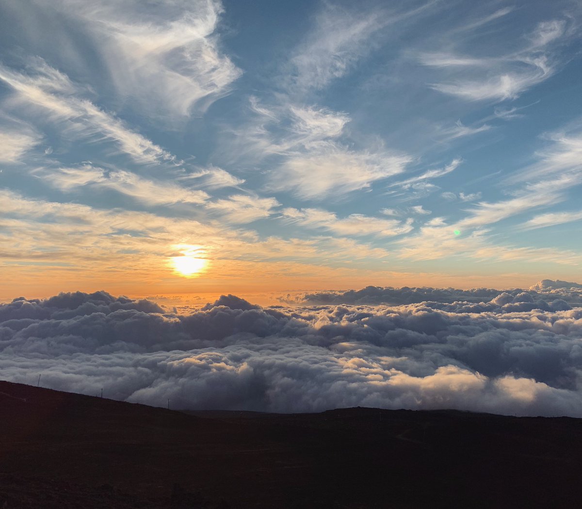 A glistening sun setting above a bunch of fluffy clouds.