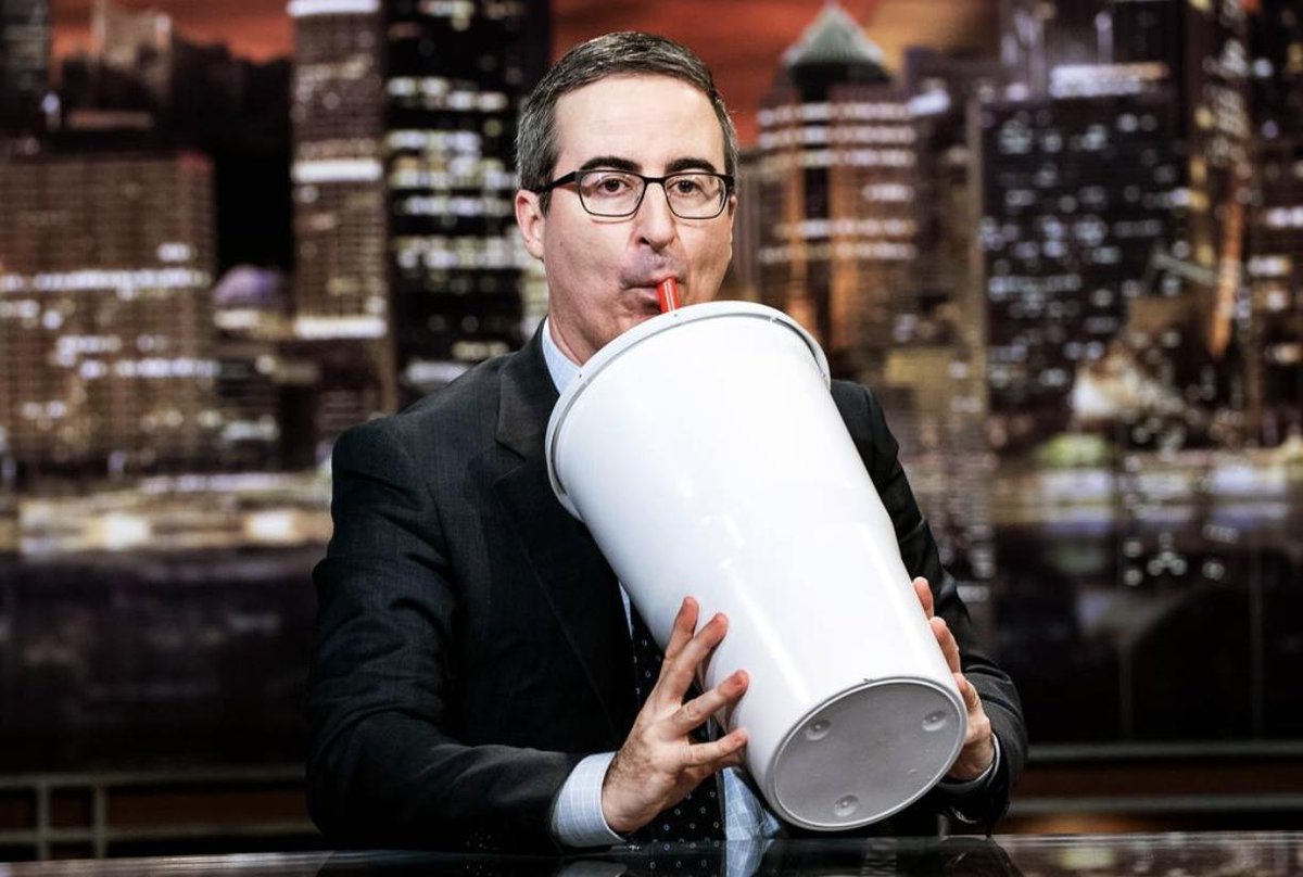 John Oliver drinking a comically giant Big Gulp soda.