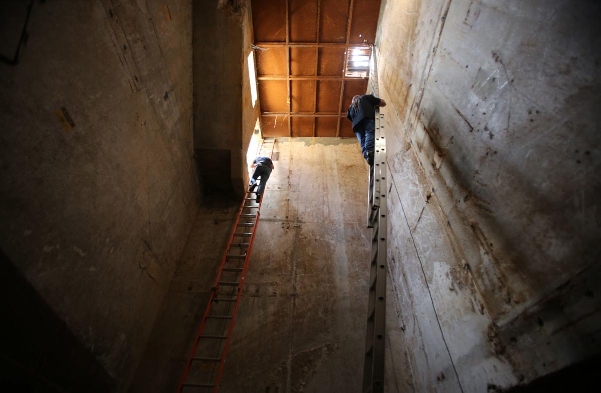 Two men standing on very tall ladders in a big concrete shaft.