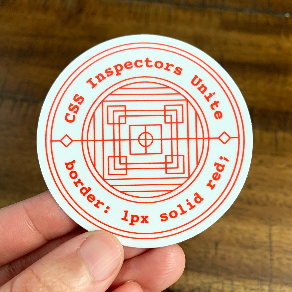 A circle vinyl sticker that says “CSS Inspectors Unite” and “border: 1px solid red;” around a circle of intercrossing, geometric red lines.