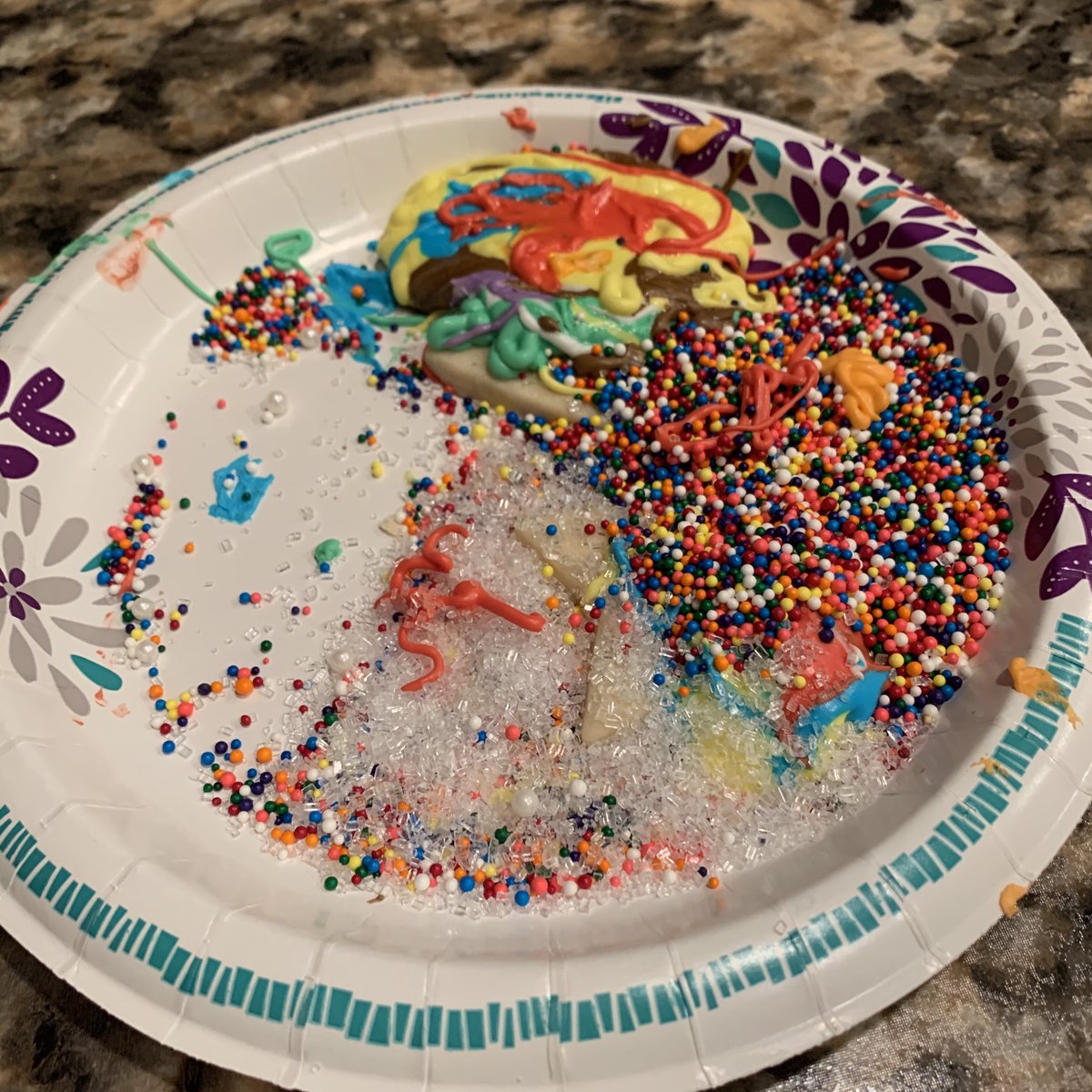 A paper plate with two cookies hidden underneath generous piles of icing and sprinkles.