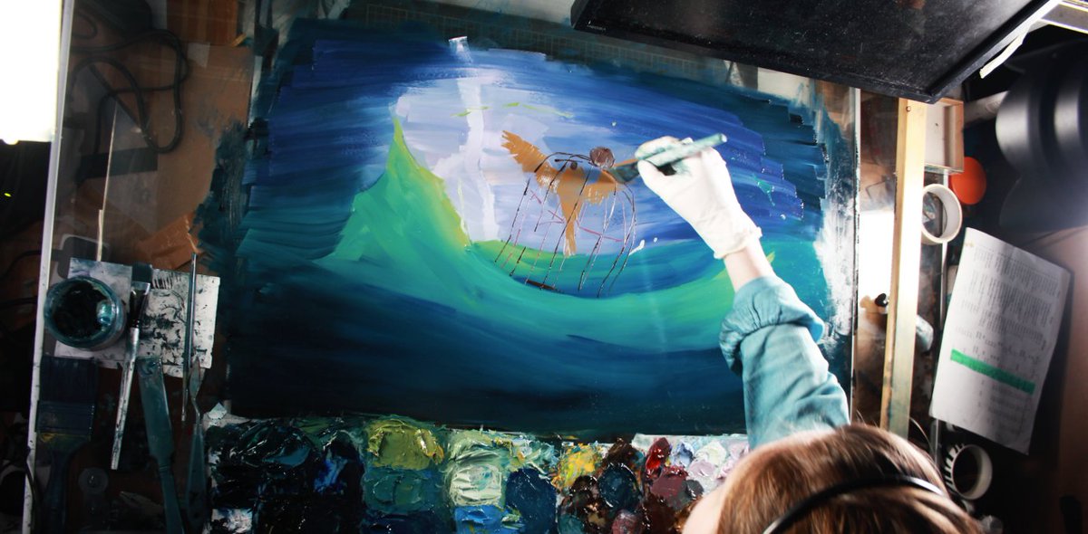 An artist painting on glass: a caged bird floating among ocean waves.