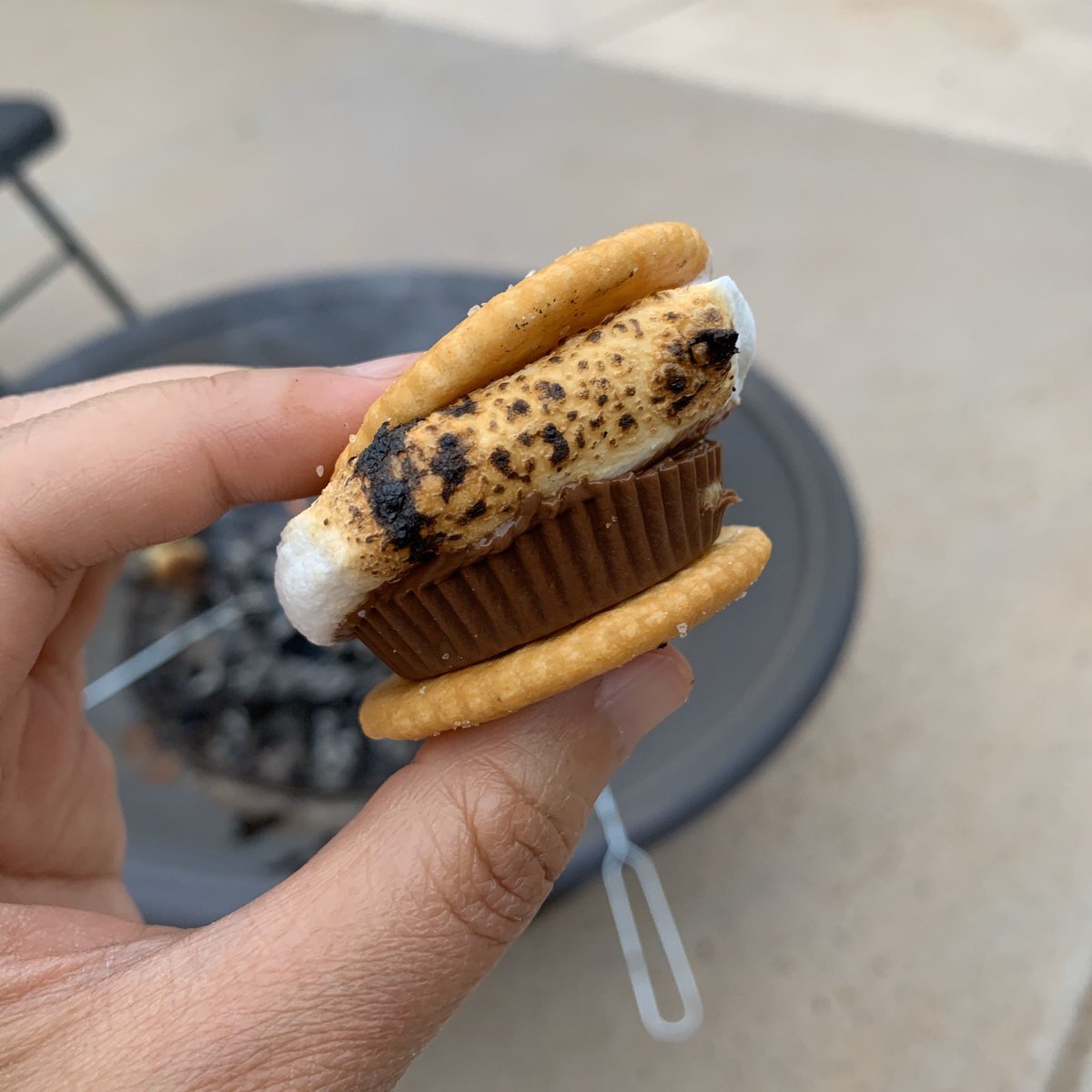 A toasty marshmallow on two Ritz crackers and a peanut butter cup. A fire pit in the background.