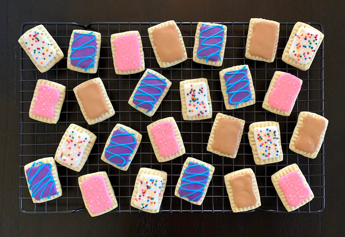 A bunch of sugar cookies decorated like pop tarts: strawberry frosted, cherry, cinnamon, and wild berry.