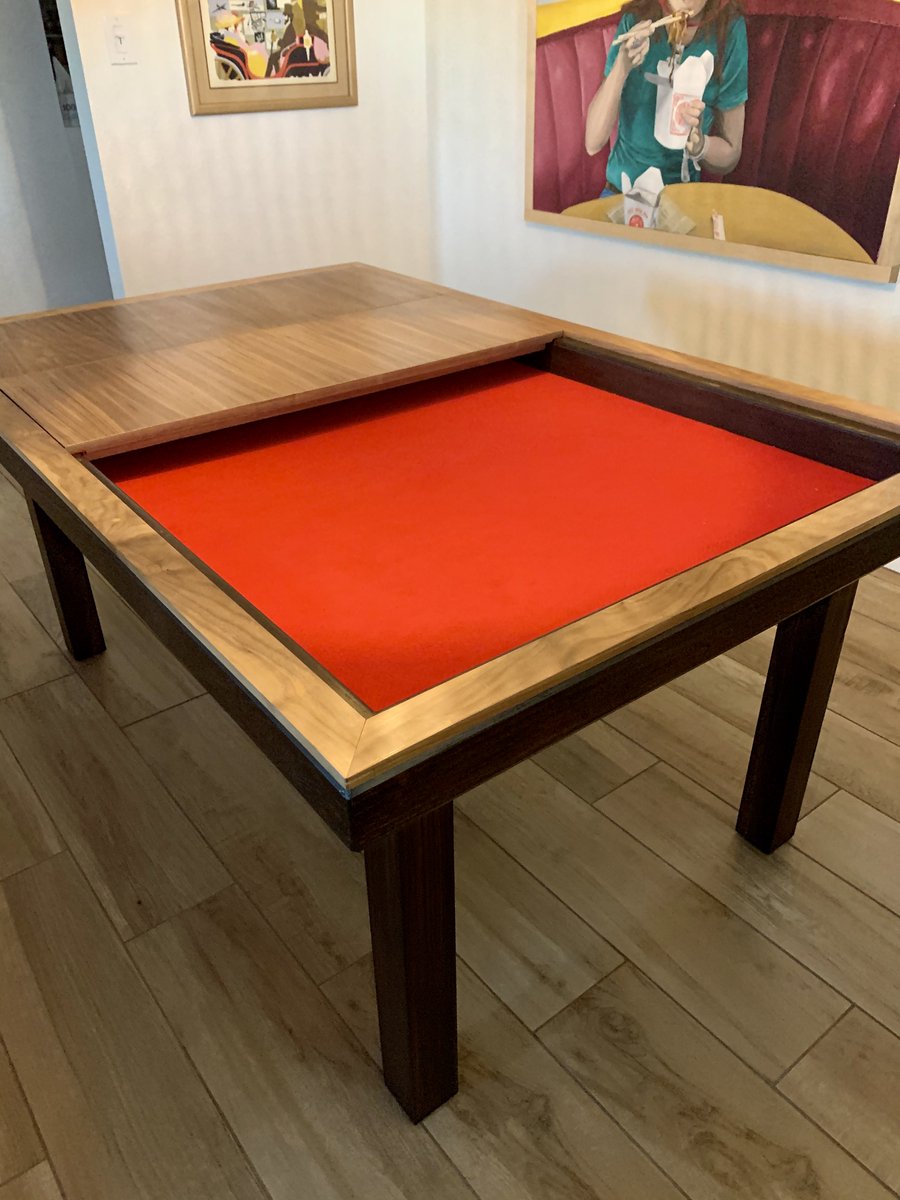 A wood dining table with part of its top removed to show a felted game surface underneath.