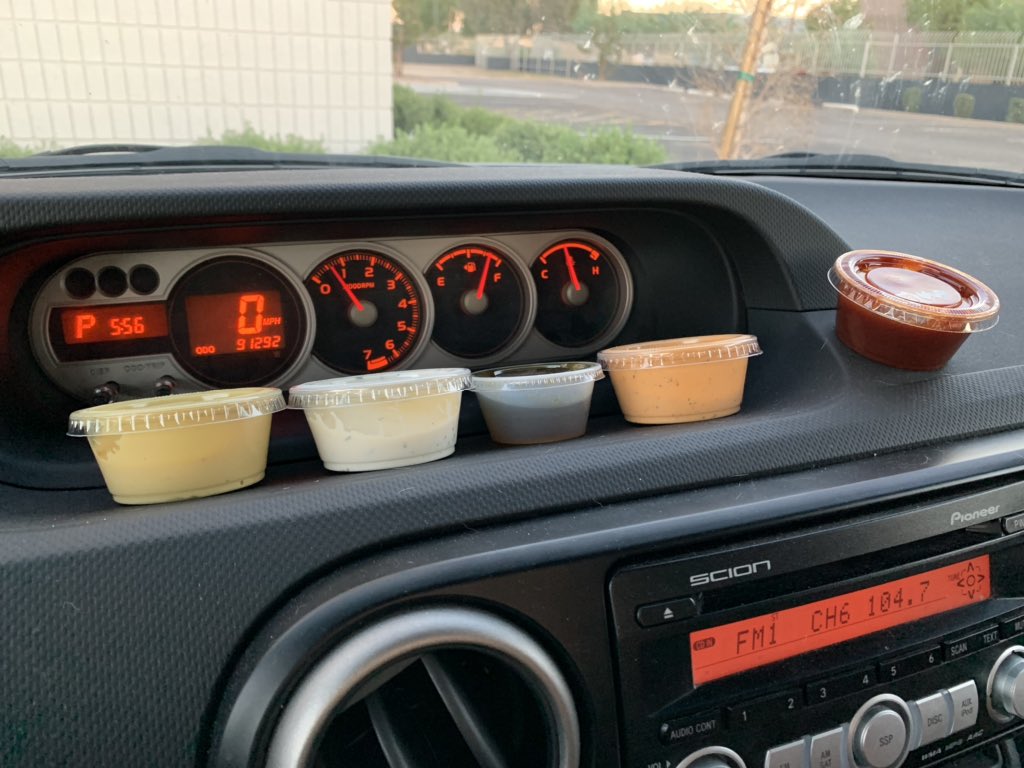 Dashboard of a car with five to-go containers of various dipping sauces.