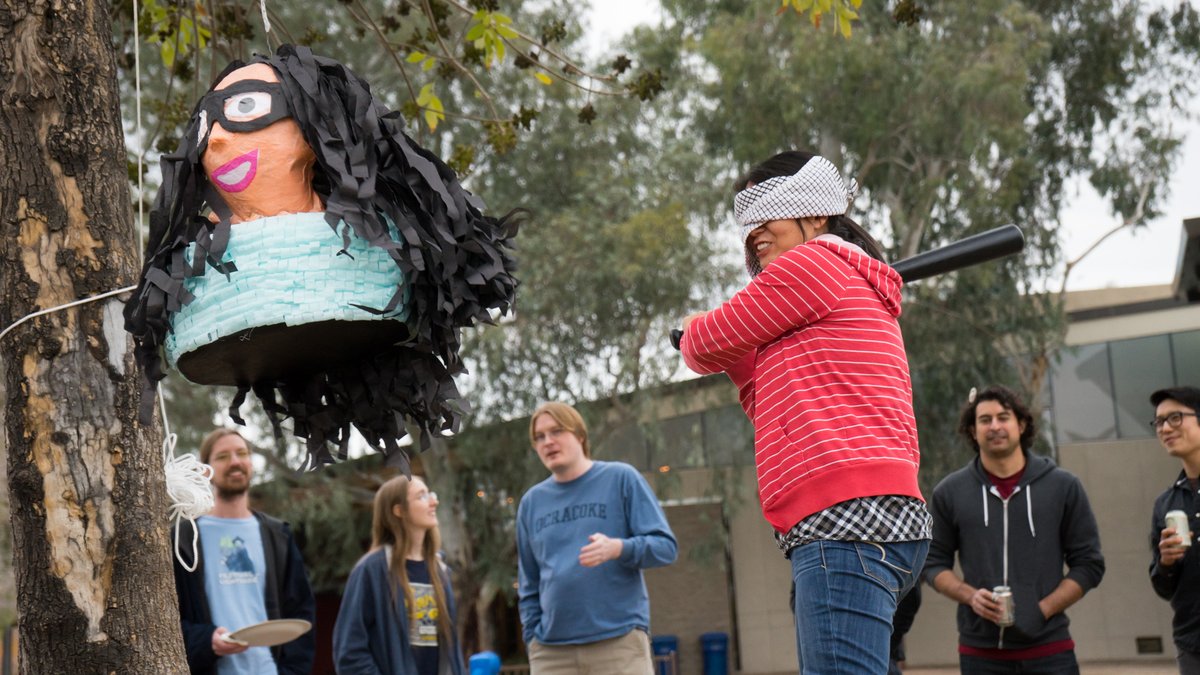 a blindfolded Lynn Fisher swings a baseball bat at a piñata that looks just like her