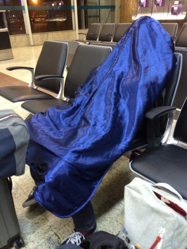 the author slouching in an airport seat, hiding under a shiny blue blanket