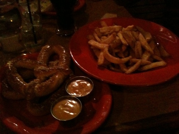 dimly-lit picture of a big soft pretzel and plate of fries