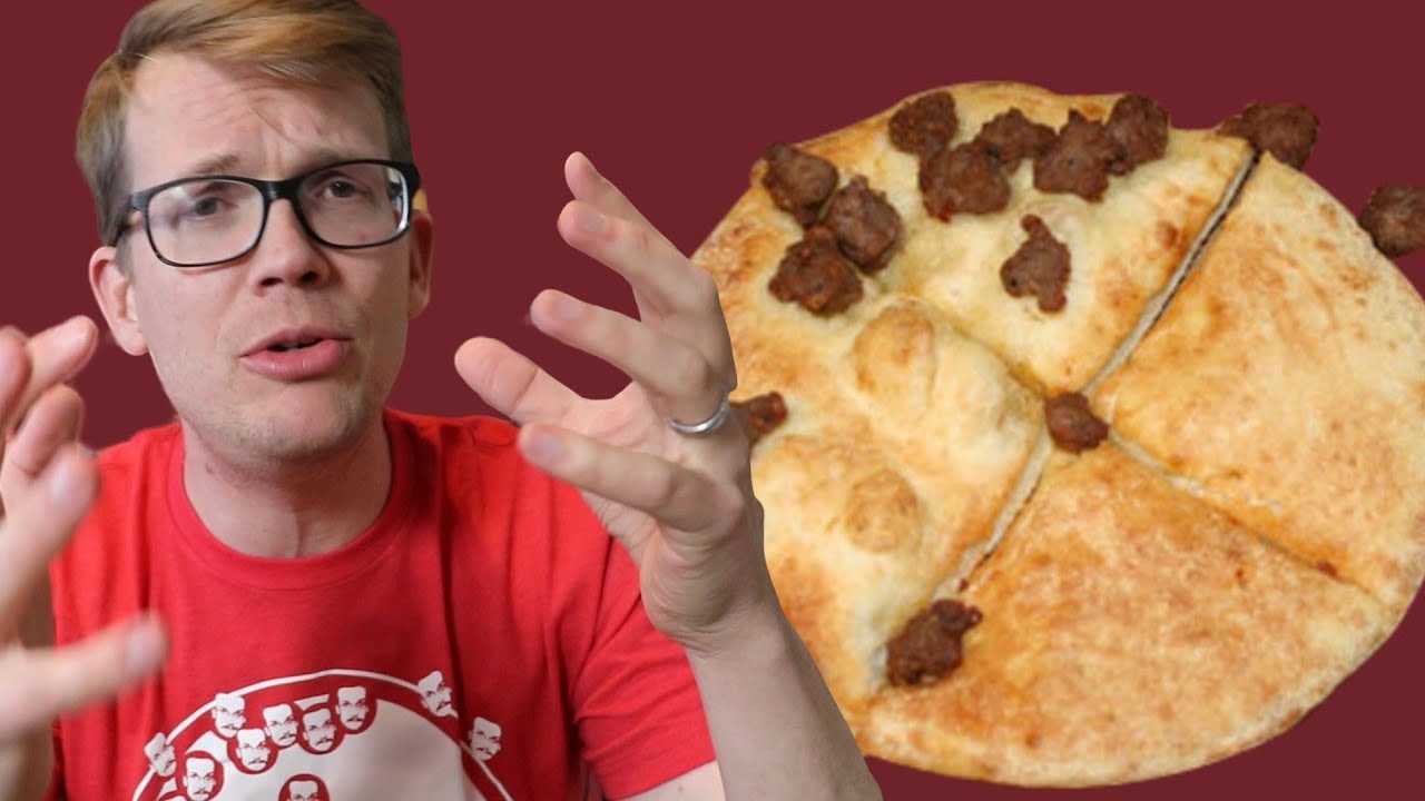 Hank Green next to a pizza with no cheese or sauce half covered in ground beef