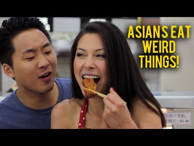 Asian man looks at an Asian woman eating food with chopsticks