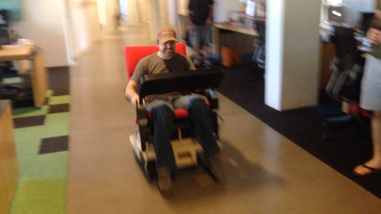 man driving an IKEA chair through an office